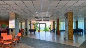 A spacious lobby with a reception desk, directional signs to the restaurant and reception, and a view of the outdoors. - Ambassador Hotel (Golden Sands)