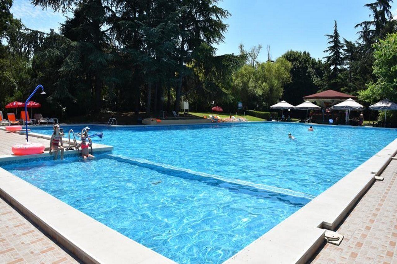 A swimming pool with clear blue water, surrounded by trees and shaded by umbrellas.