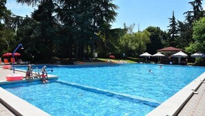 A swimming pool with clear blue water, surrounded by trees and shaded by umbrellas. - Ambassador Hotel (Golden Sands)
