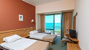 A hotel room with two beds, a desk with a TV, a chair, and a view of the ocean. - Ambassador Hotel (Golden Sands)