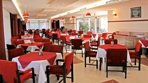 Un restaurant avec des chaises et des tables rouges, un espace cuisine et de grandes fenêtres.