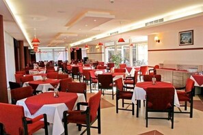 Un restaurante con sillas y mesas rojas, una zona de cocina y ventanas grandes.