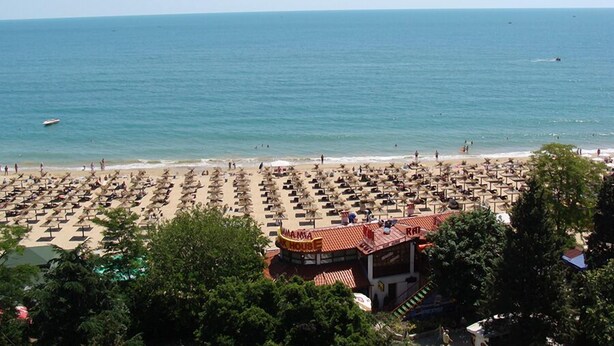 A beach with rows of sunbeds and umbrellas, a building labeled "MAJOLA HOUSE" with a red roof, and the ocean in the background. - Ambassador Hotel (Golden Sands)