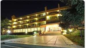 A multi-story hotel with a well-lit entrance and a landscaped garden area. - Ambassador Hotel (Golden Sands)