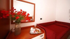 A hotel room with a wooden bedside table, a vase of red flowers, a tray with bread and a jug, and a red sofa. - Hotel Ardesia (Rimini)