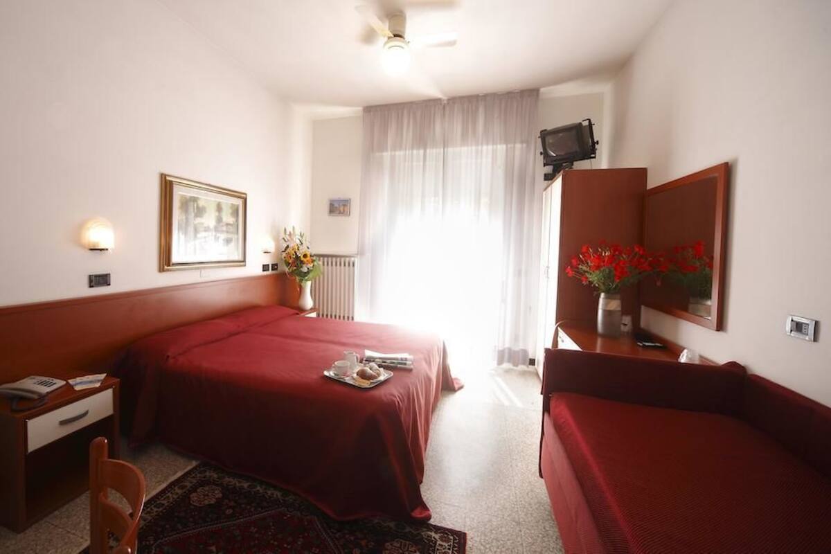 A hotel room with two beds, a desk, a chair, a TV, and a window with curtains.