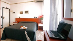 A hotel room with a bed, a desk with a laptop, a nightstand, a bedside table, a mirror, and a window with curtains. - Hotel Ardesia (Rimini)