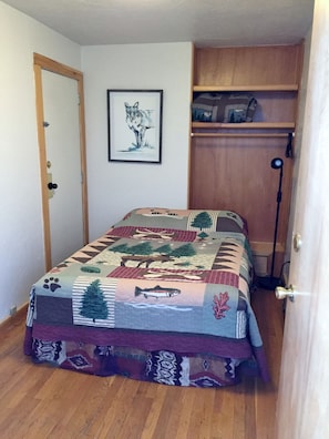 A bedroom with a bed, a door, a framed picture on the wall, and a shelf with items. - Kineo View Lodge (Greenville)