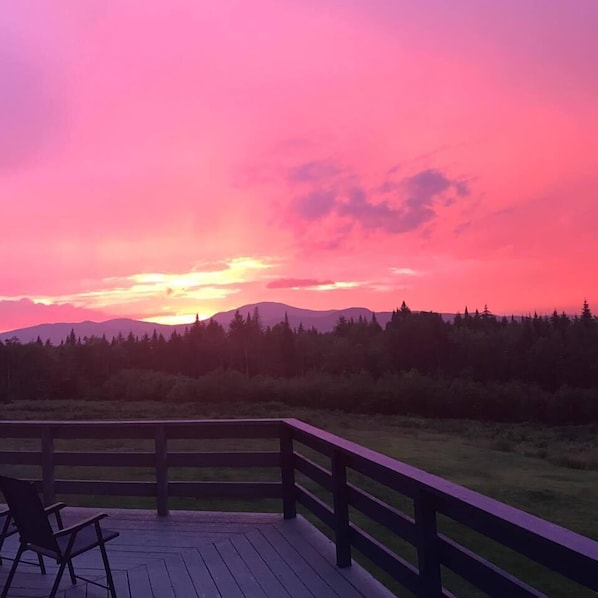 A wooden deck with a railing overlooking a forested landscape during sunset. - Kineo View Lodge (Greenville)