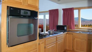 A kitchen with wooden cabinets, a stainless steel oven, a microwave, and a window with curtains. - Kineo View Lodge (Greenville)