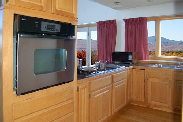 A kitchen with wooden cabinets, a stainless steel oven, a microwave, and a window with curtains. - Kineo View Lodge (Greenville)