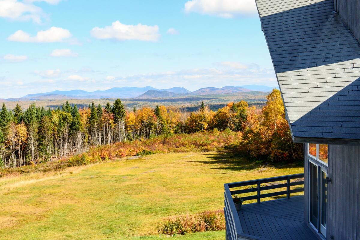 A house with a deck overlooking a grassy field and a forest.