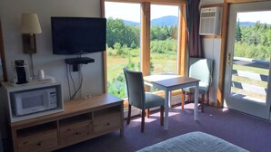 A hotel room with a bed, a TV, a microwave, a table, and chairs. - Kineo View Lodge (Greenville)