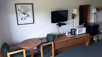 Ett hotellrum med en tv, en kaffebryggare, en mikrovågsugn, ett litet bord, två stolar och ett inramat konstverk på väggen.