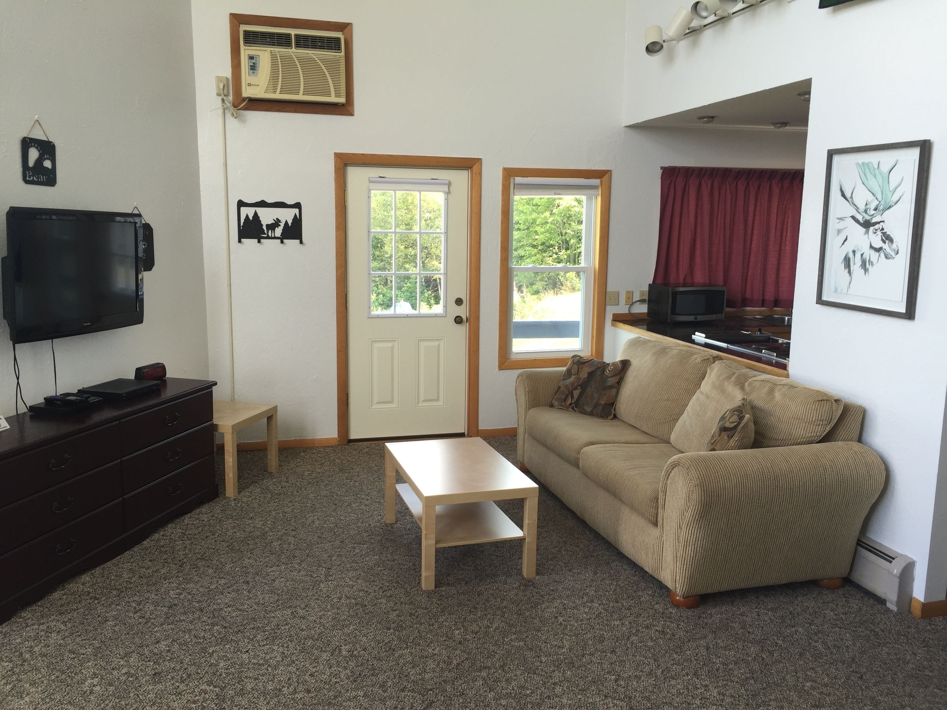 A living room with a TV, a sofa, a coffee table, and two windows.