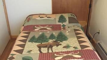 A bed with a patterned blanket, a framed picture on the wall, and a wooden shelf with items.