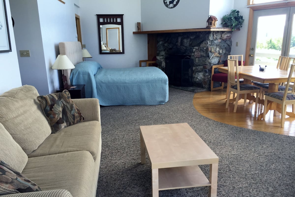 A living room with a beige sofa, a blue sofa, a wooden coffee table, and a dining area with a wooden table and chairs.