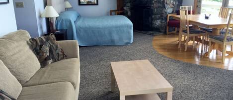 Un salon comprenant un canapé beige, un canapé bleu, une table basse en bois et un coin repas avec une table et des chaises en bois.