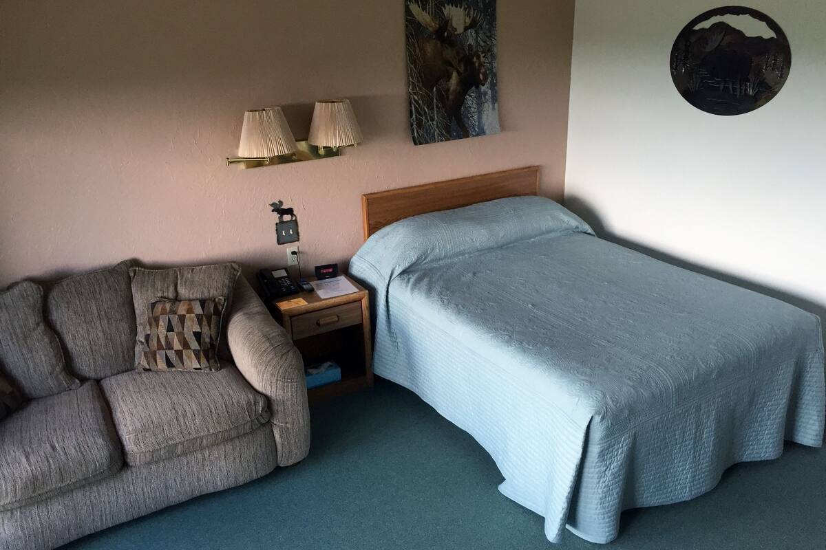 A bedroom with a bed, a nightstand, a lamp, a wall clock, and a framed picture.