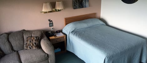 A bedroom with a bed, a nightstand, a lamp, a wall clock, and a framed picture.