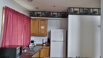 A compact kitchen with wooden cabinets, a white refrigerator, a microwave, and a coffee maker.