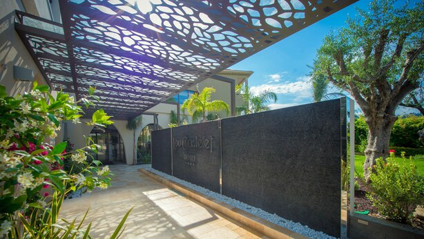 A hotel entrance with a modern design, featuring a pathway lined with white pebbles and a decorative metal canopy. - Hôtel Lou Castelet (Carros)