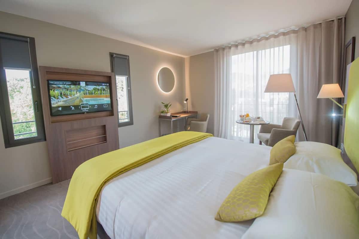 A hotel room with a bed, a desk, a chair, a TV, and a lamp.