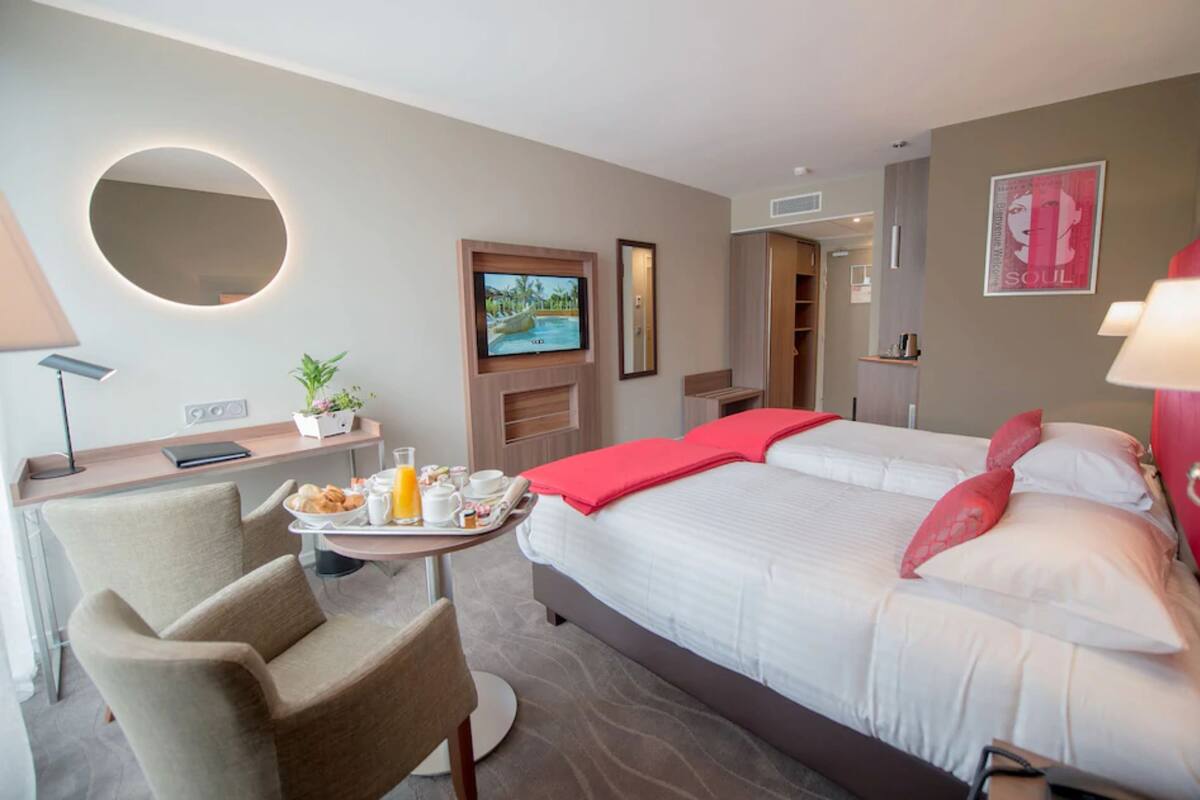 A hotel room with a bed, a desk with a chair, a TV, a mirror, and a breakfast tray.