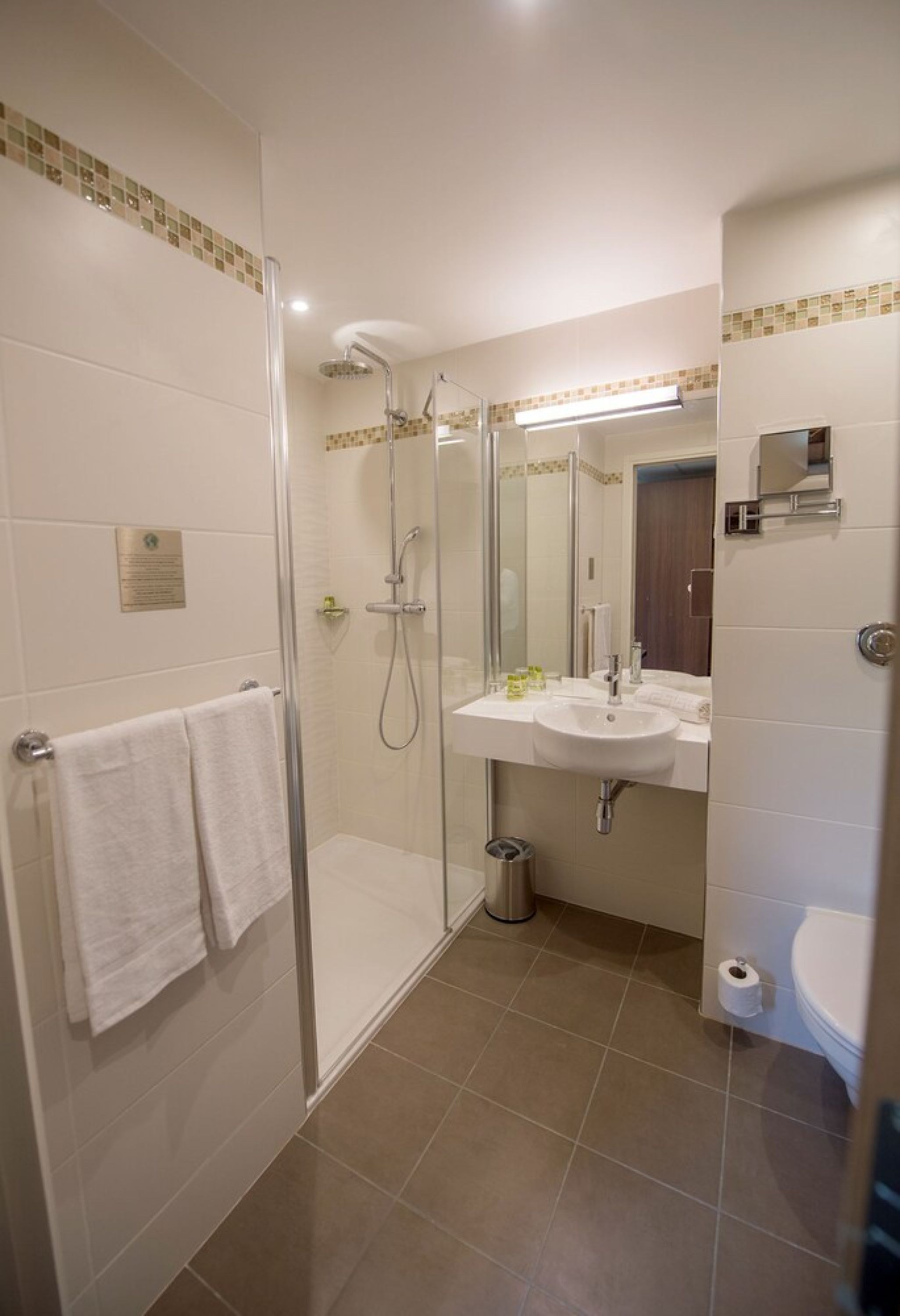 Un baño con ducha de vidrio, lavamanos con espejo e inodoro.