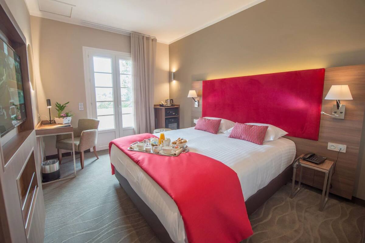 A hotel room with a large bed, a desk, a chair, a TV, and a window.