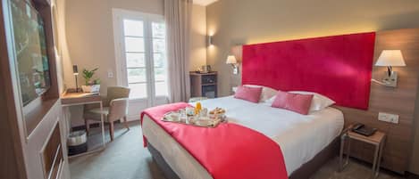 A hotel room with a large bed, a desk, a chair, a TV, and a window.