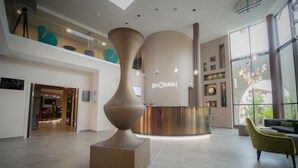 A modern lobby with a reception desk, a large sculptural centerpiece, and a seating area with yellow chairs. - Hôtel Lou Castelet (Carros)