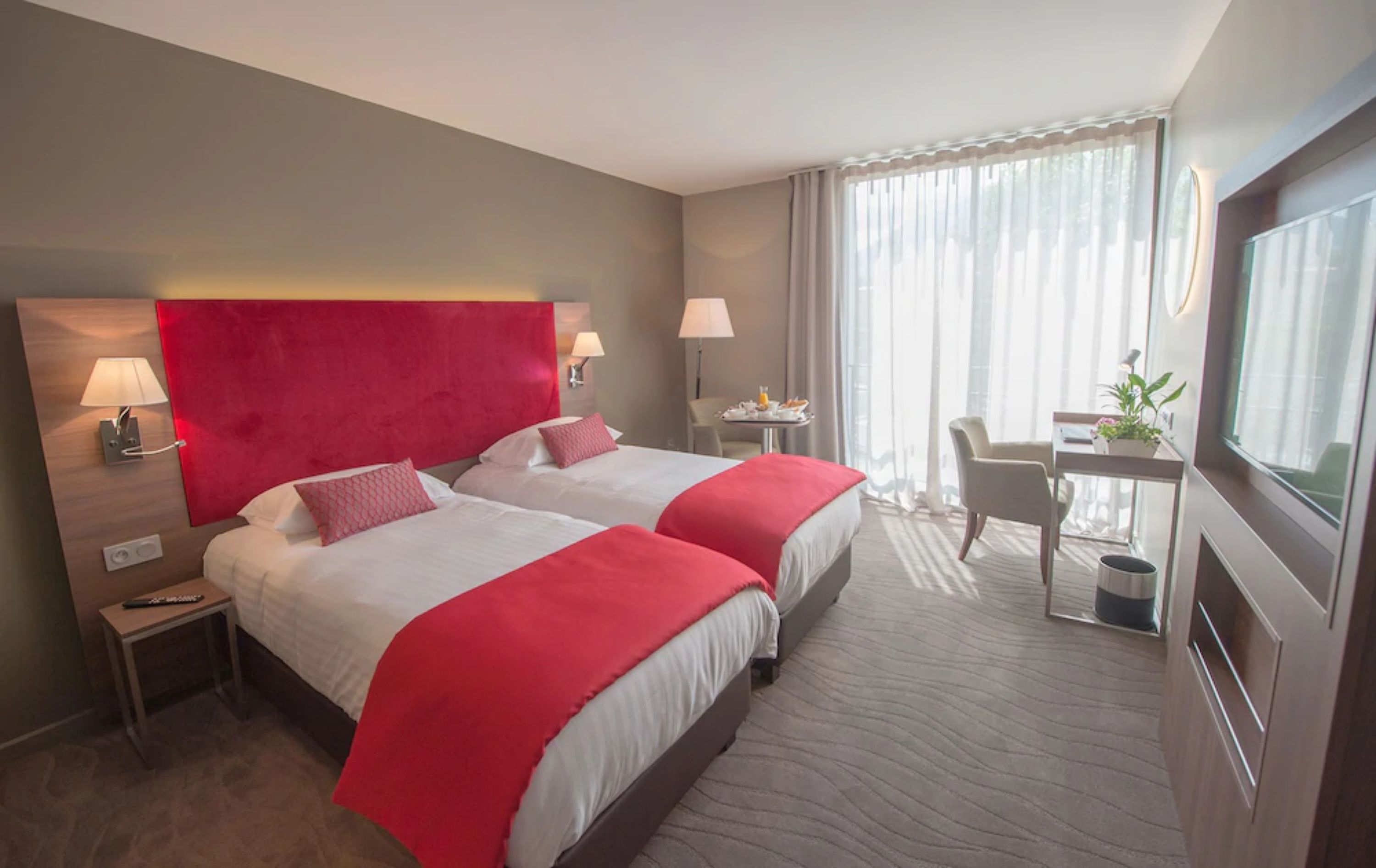 A hotel room with two beds, a desk, a chair, and a TV.