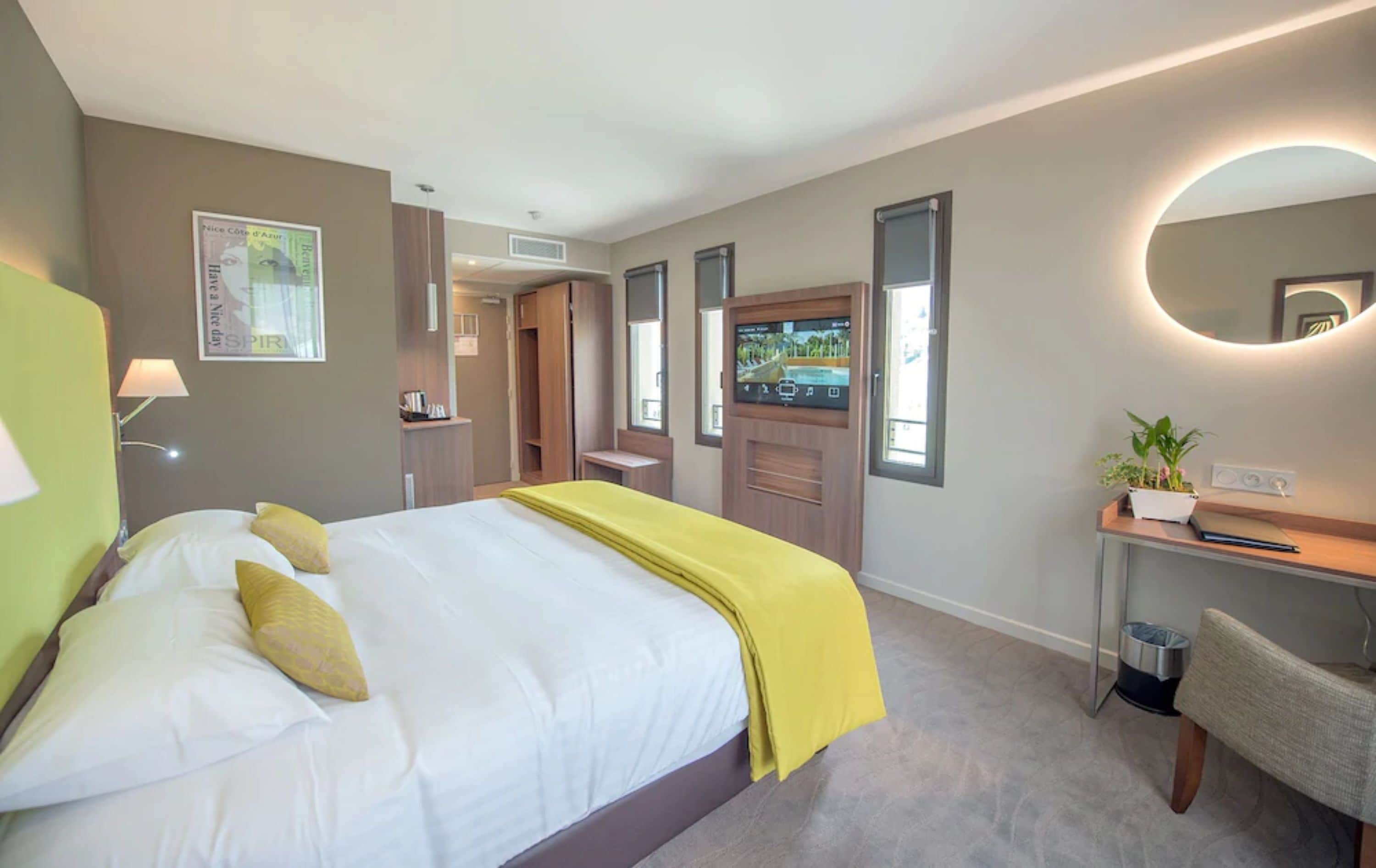 Habitación de hotel con una cama, un escritorio, una silla, un espejo y un televisor.