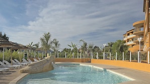 A swimming pool with a stone waterfall feature, surrounded by lounge chairs and a palm tree-lined area. - Hôtel Lou Castelet (Carros)