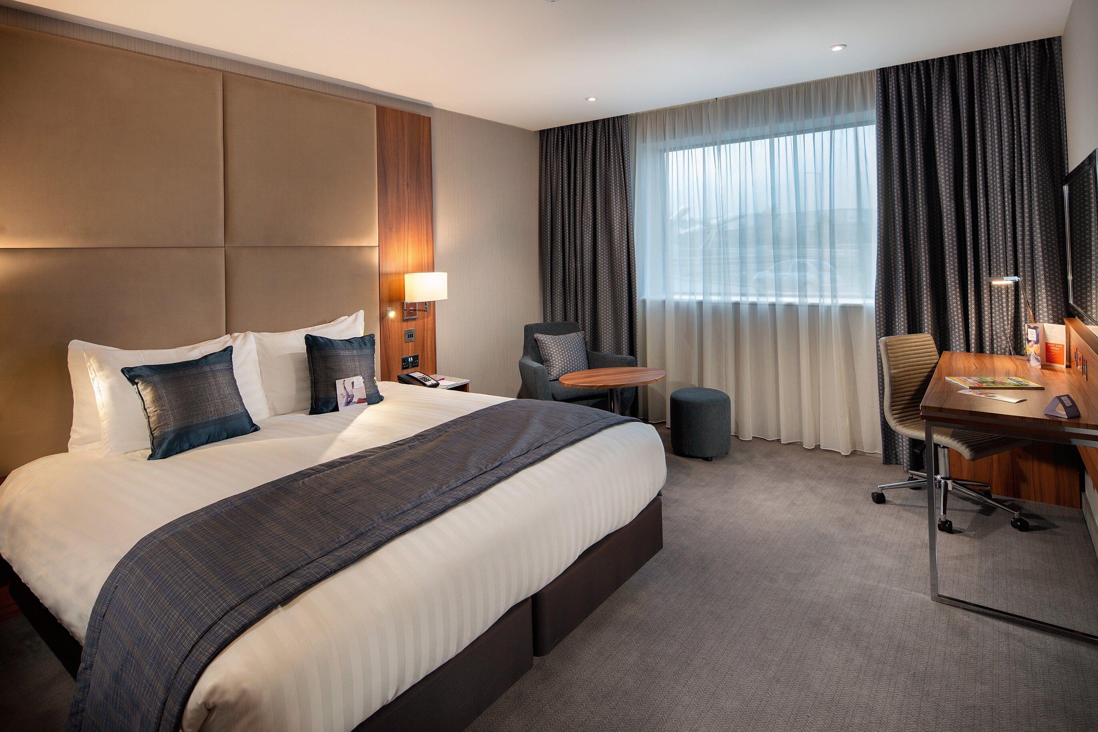 Une chambre d’hôtel avec un grand lit, un bureau, une chaise, une petite table, une lampe et un téléviseur.
