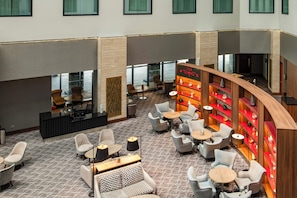 A hotel lobby with multiple seating areas, a reception desk, and a bar area with shelves. - Crowne Plaza London Heathrow T4 by IHG (Hounslow)