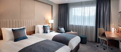 A hotel room with two beds, a desk, a chair, and a small round table.