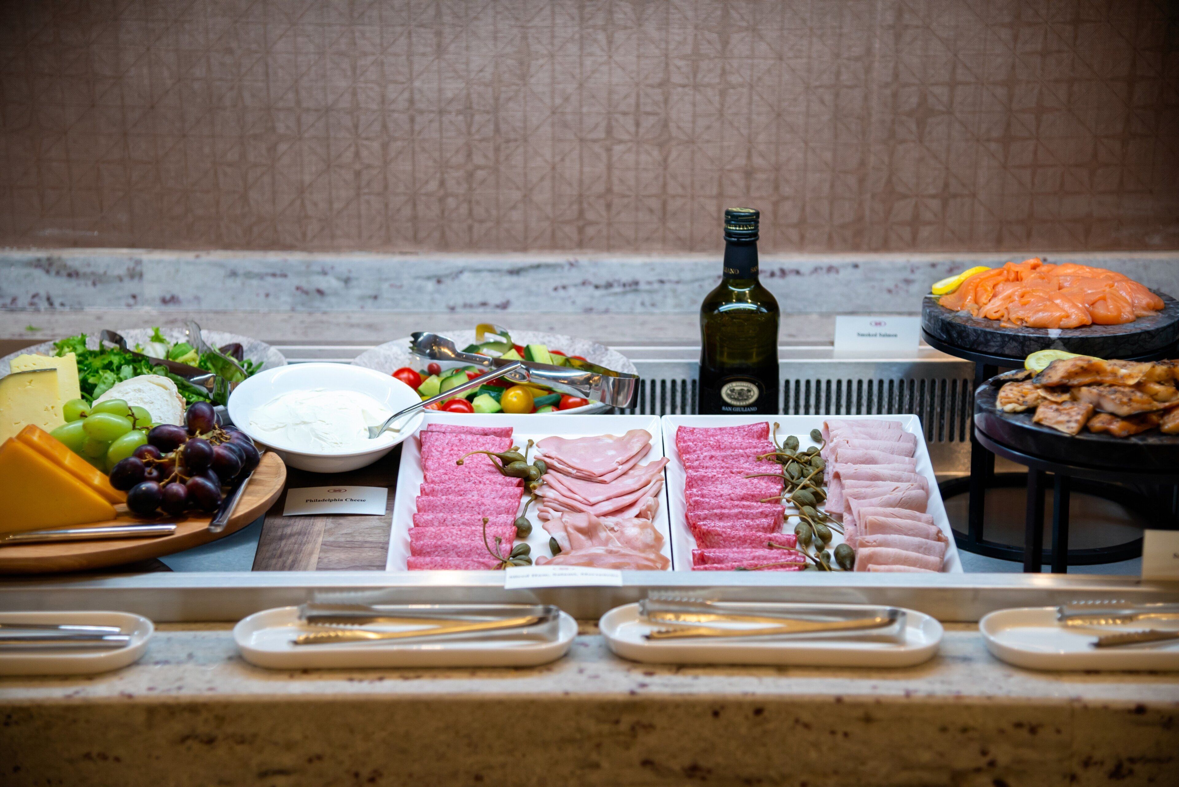 A buffet table with various food items including cheese, meats, and a bottle of wine.