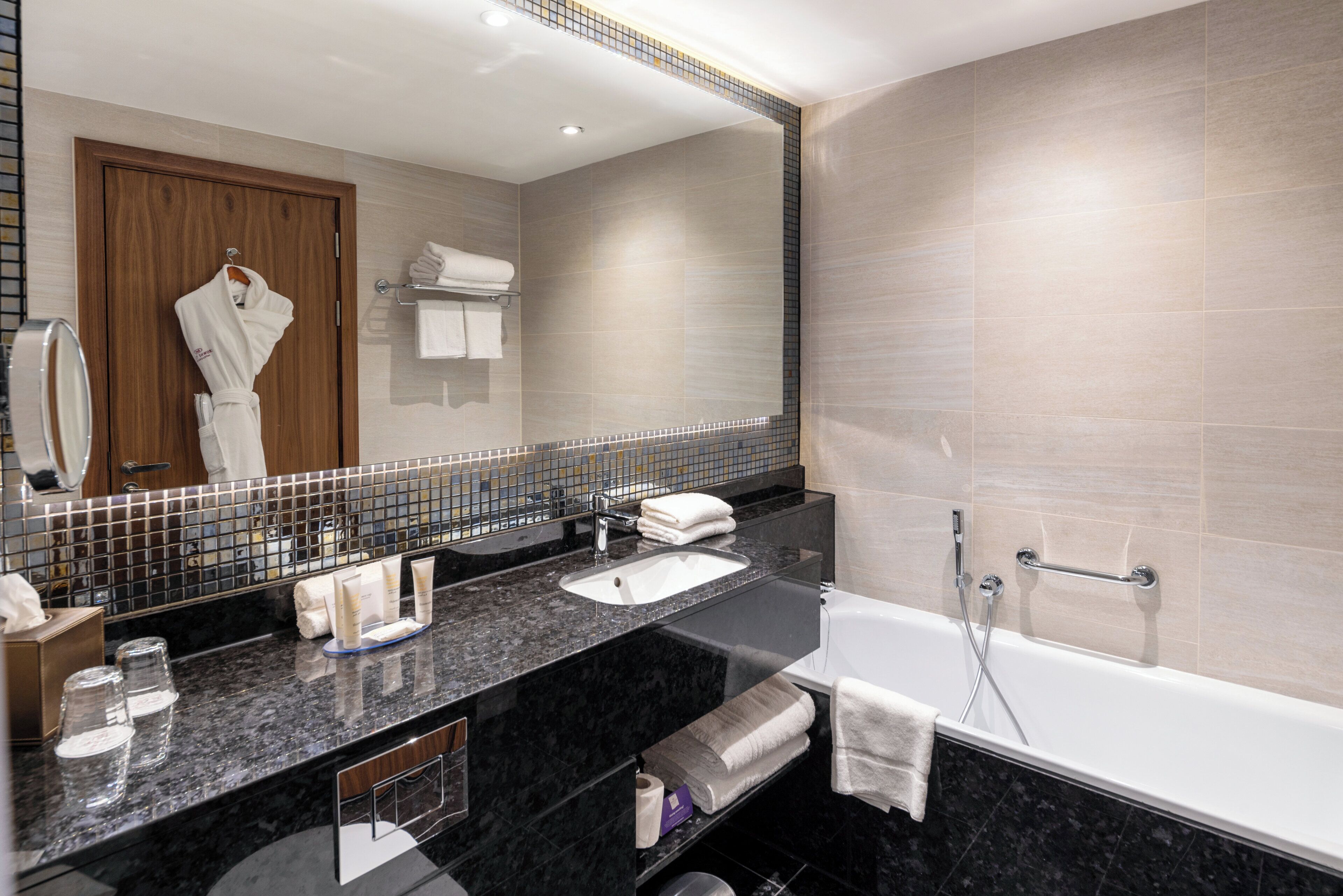 A modern bathroom with a large mirror, a bathtub, a sink, and a vanity area.