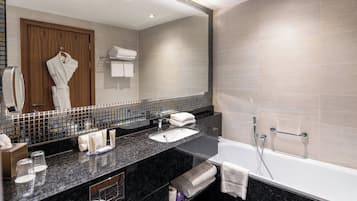 A modern bathroom with a large mirror, a bathtub, a sink, and a vanity area.
