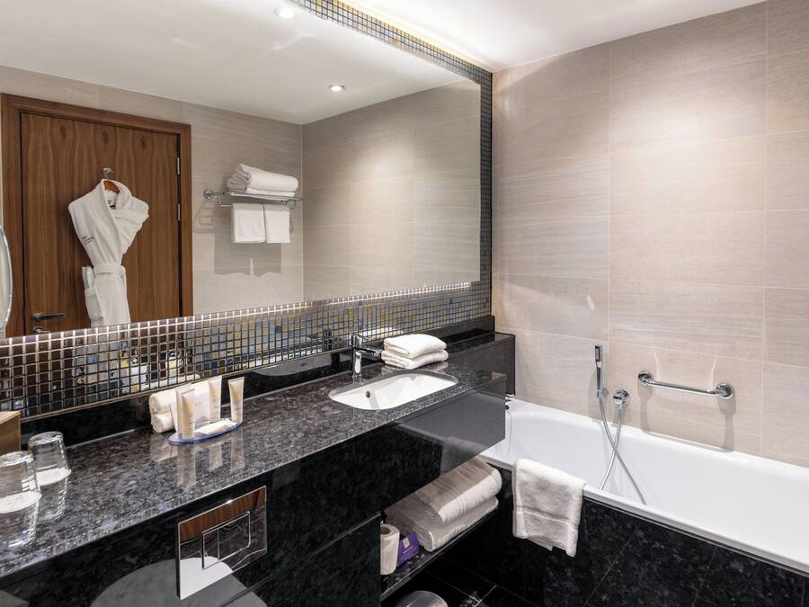 A modern bathroom with a large mirror, a bathtub, a sink, and a vanity area.