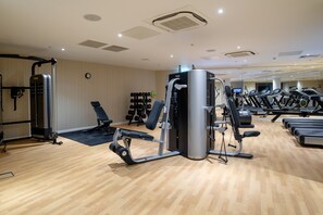 Un gimnasio con diverso equipo de ejercicio, incluyendo cintas de correr y máquinas de pesas, y piso de madera.