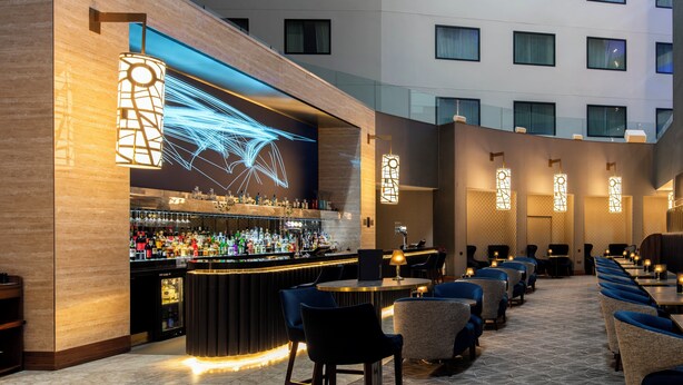 A bar area with a long counter, multiple seating options, and a large illuminated screen. - Crowne Plaza London Heathrow T4 by IHG (Hounslow)
