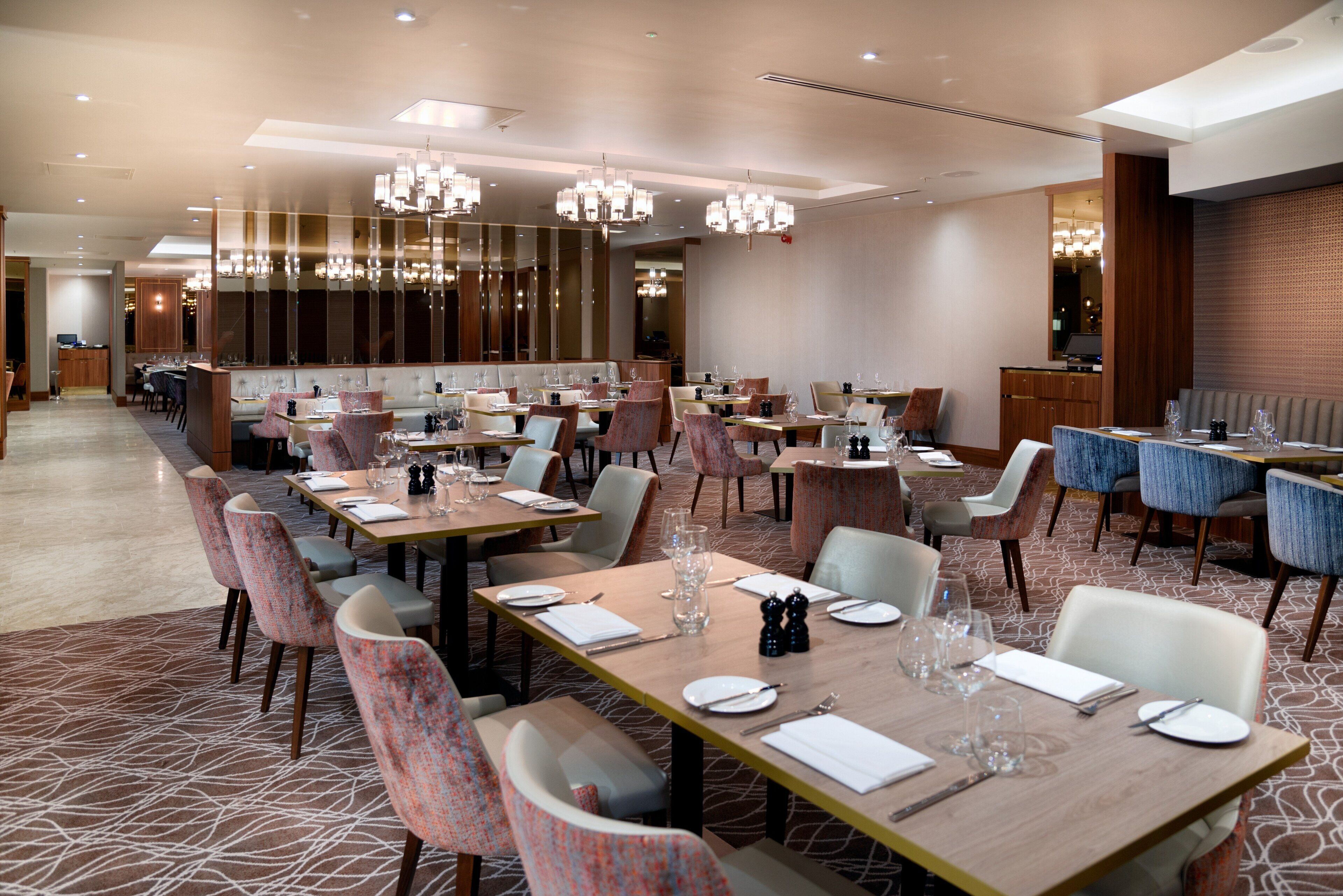 A spacious dining area with multiple tables and chairs, elegant chandeliers, and a modern interior design.
