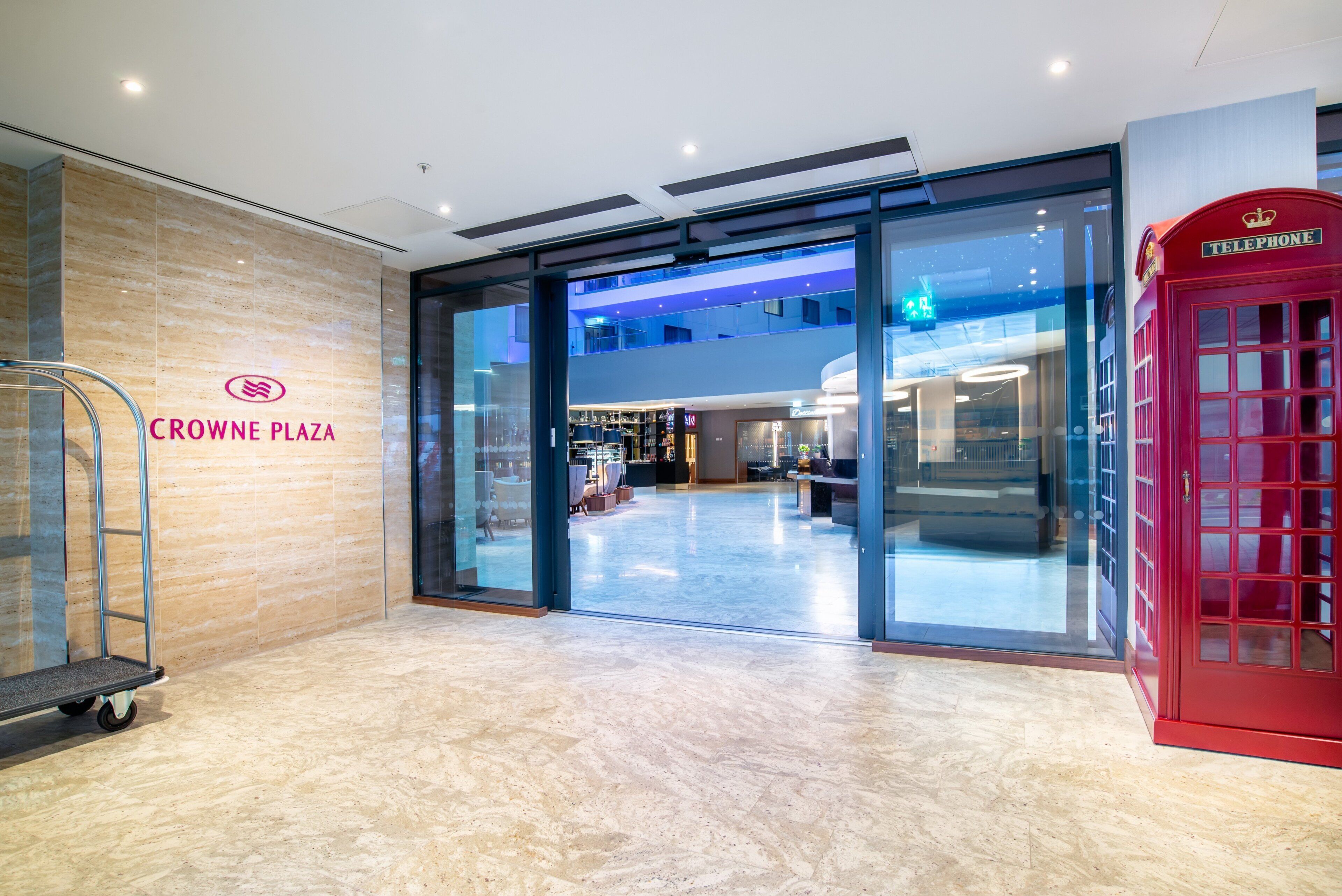 A modern interior with a glass entrance, a red telephone booth, and a sign for Crowne Plaza.