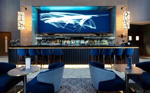 A bar area with a long counter, multiple seating options, and a large screen displaying abstract art. - Crowne Plaza London Heathrow T4 by IHG (Hounslow)