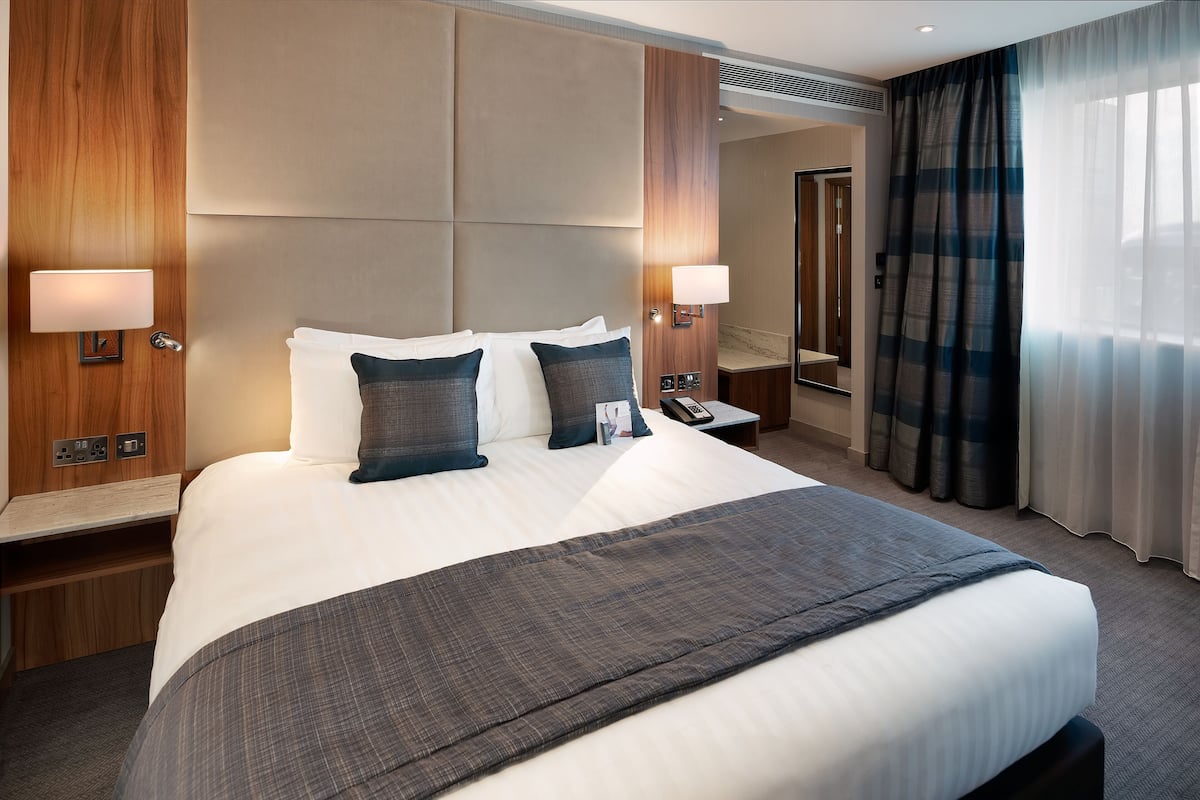A hotel room with a large bed, two bedside tables, a nightstand, a mirror, and a window with curtains.