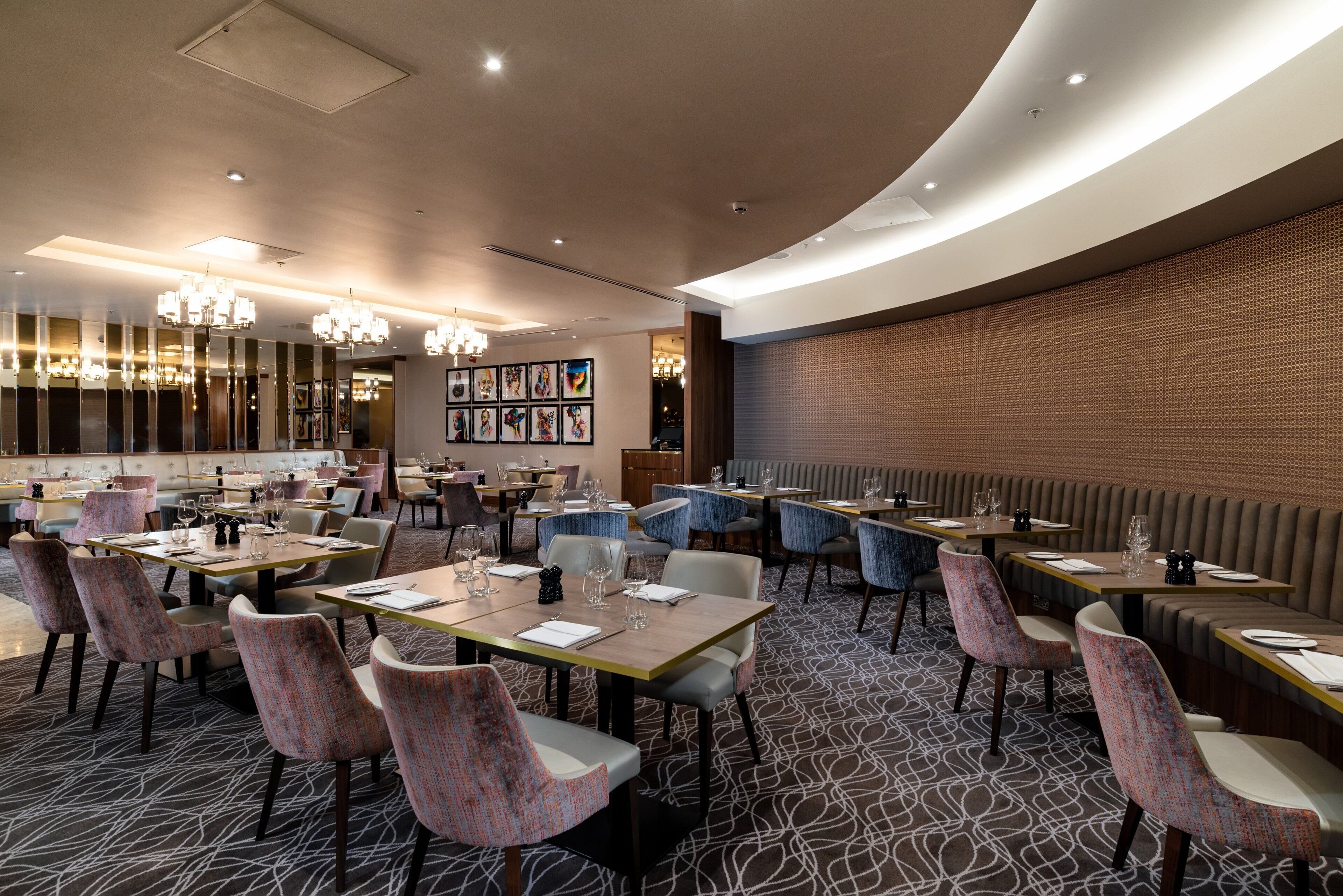 A modern restaurant with round tables, cushioned chairs, and a patterned carpet.