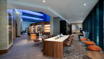 Un lobby moderno de hotel con una barra central, zonas de estar y vistas al cielo a través del techo.
